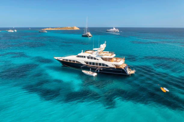 Aerial view of luxury yacht on blue sea at sunny day in summer. Sardinia, Italy. Aerial view of speed boats, yachts, sea lagoon, shore, transparent water, sky. Top view from drone. Tropical seascape